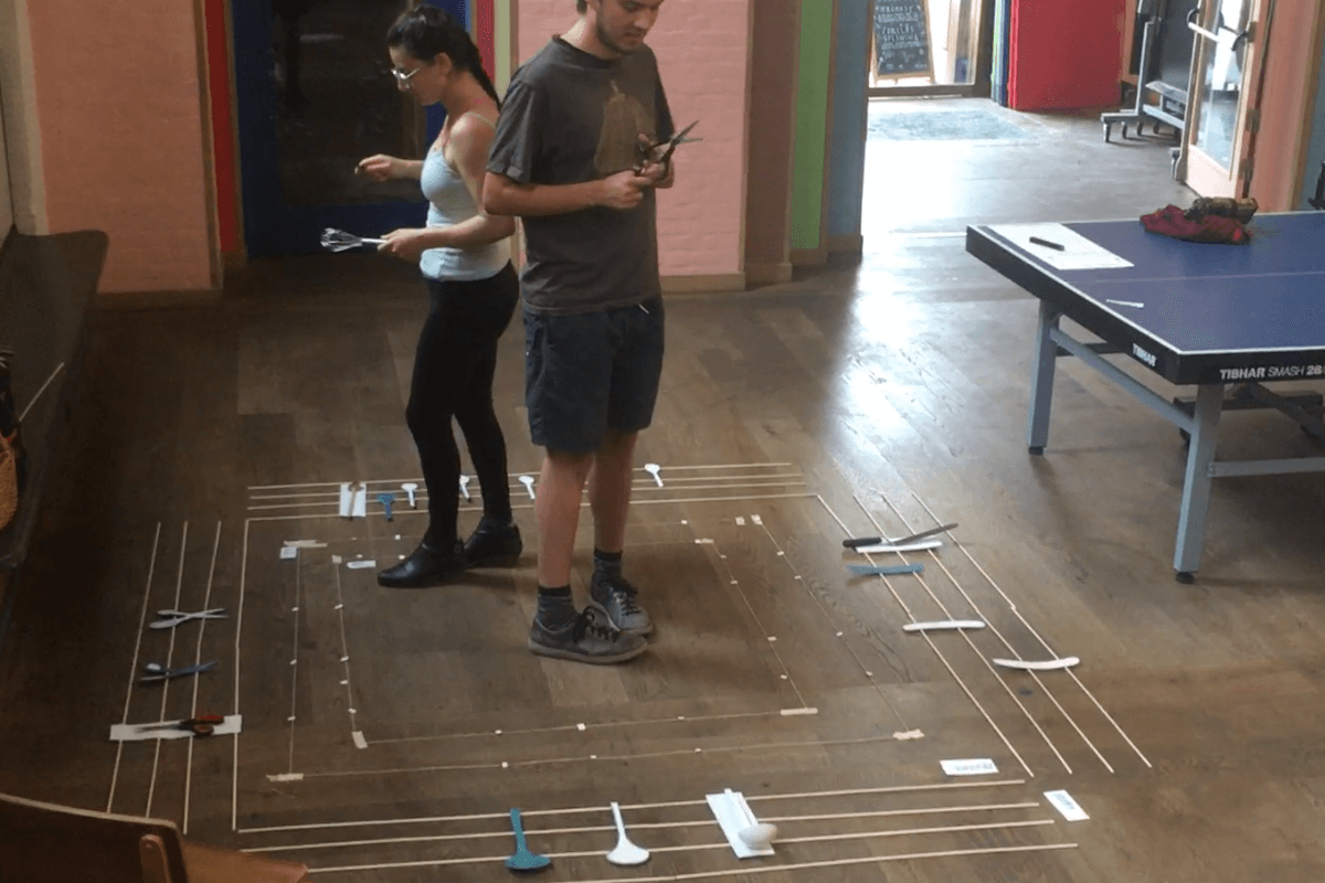 Two people inside a musical notation system drawn on the floor play kitchen tools 