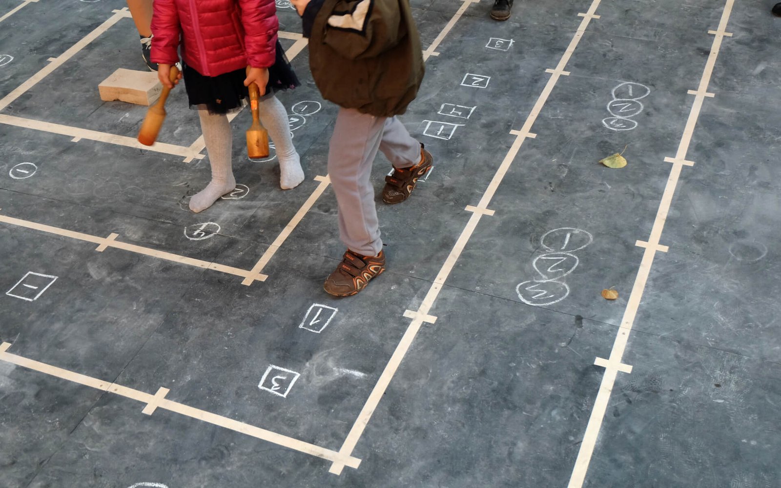 The legs 2 children holding kitchen utensils marching on a chalkboard score.