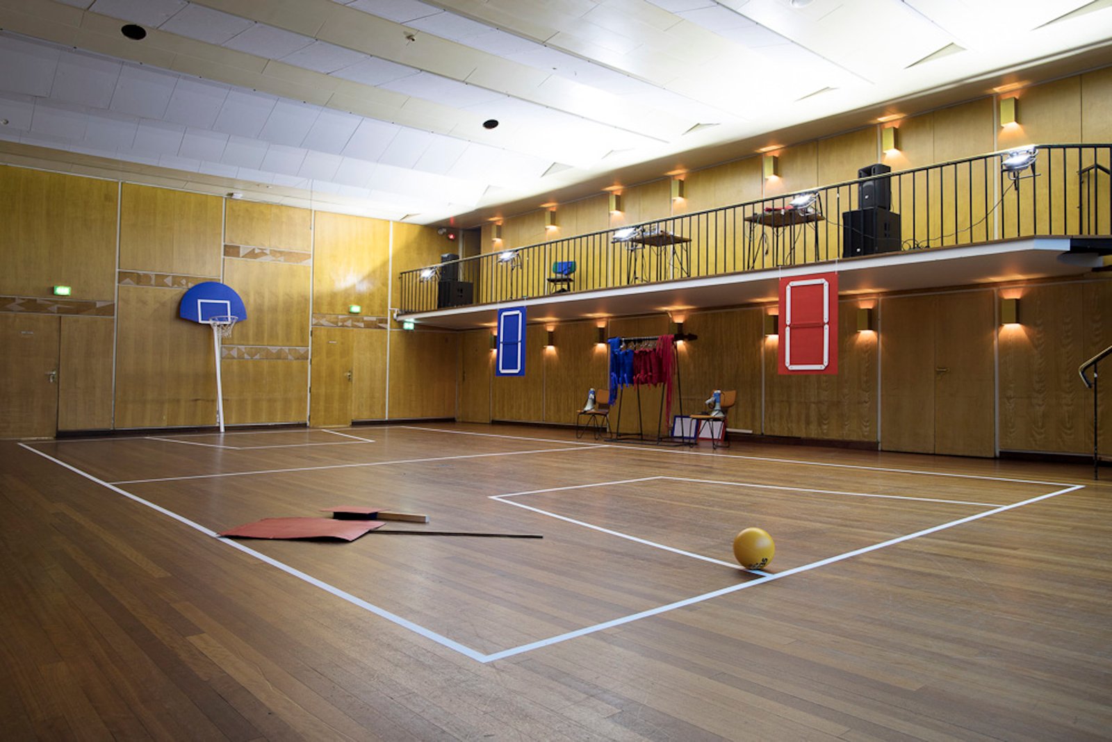 A basketball goal on a stick, score boards, costumes and picket signs in a room with wooden walls and floors and geometric decorations