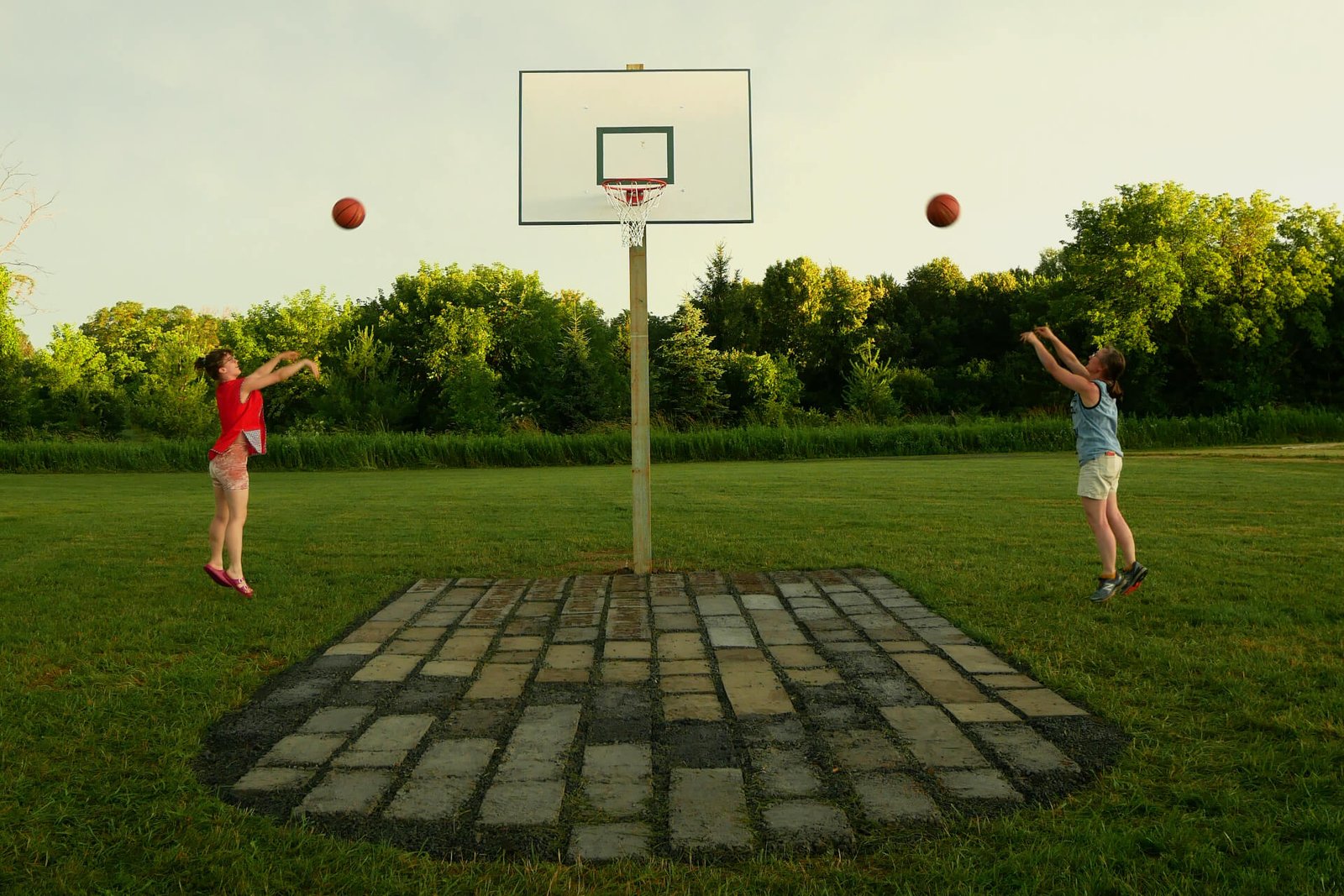 A person in blue and one in red each shoot a basketball at the dirtball hoop