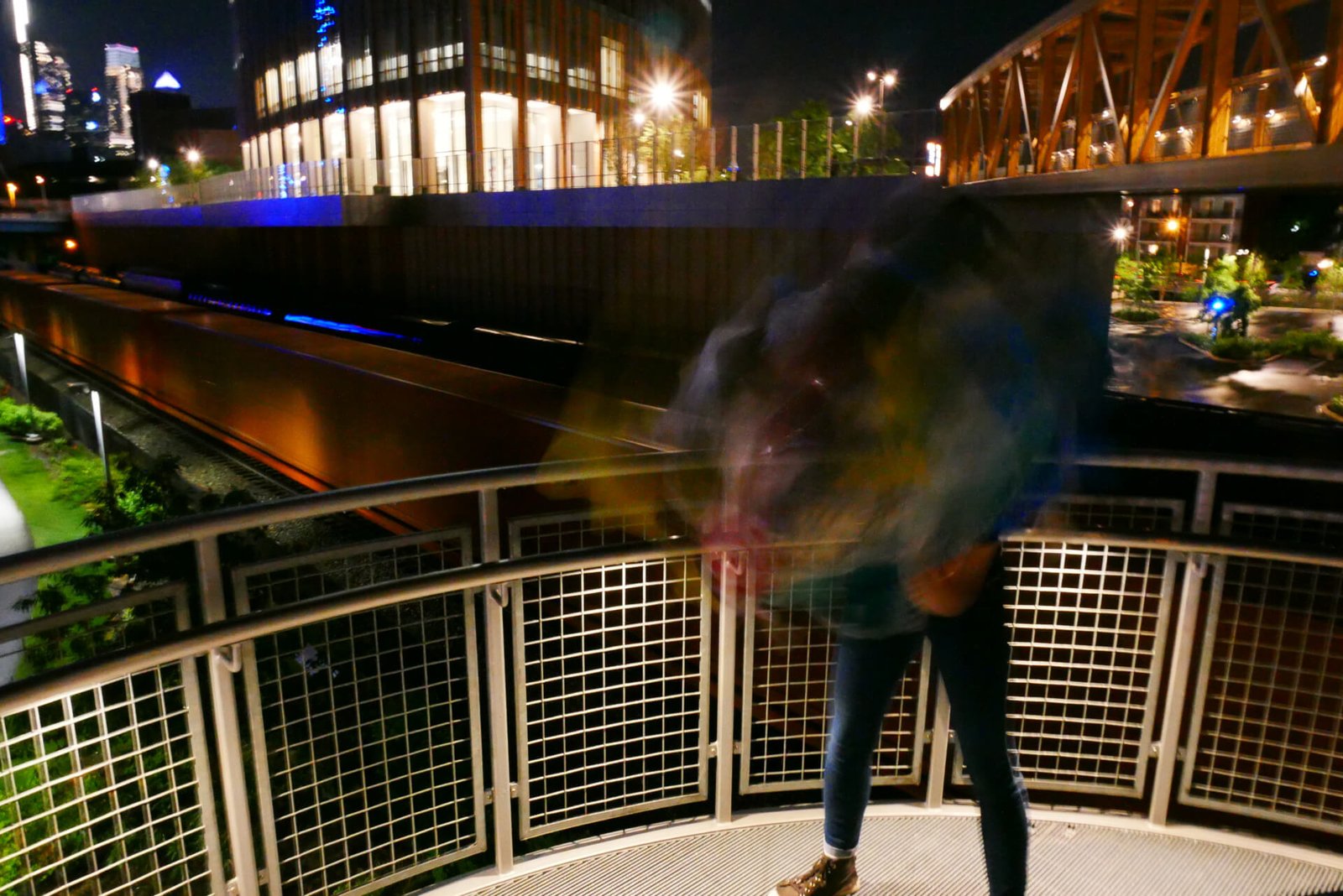 A person standing on an outdoor stairway at night wearing a Plastic Dance helmet made of trash moving their head so fast it is blurred.